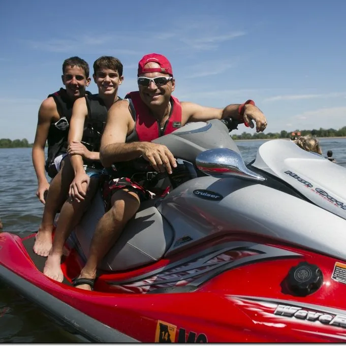 3 males on a wave runner, in the water, smiling at the camera