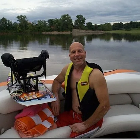 an adult male skier in the back of a boat with his ski, with a great big smile on his face