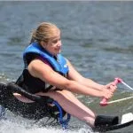 teenaged female sit skier smiling as she is holding on to the ski rope while she skis around the lake